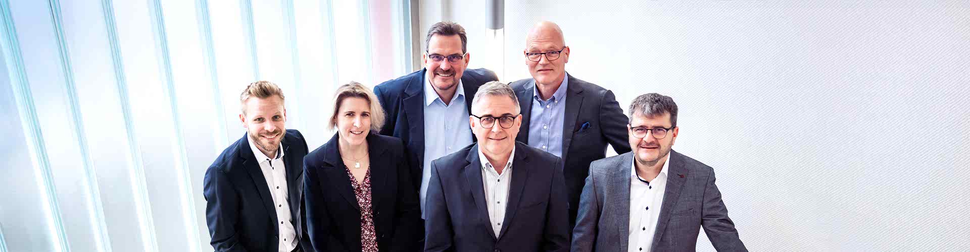 5 Personen in Sakko stehen auf einer Treppe